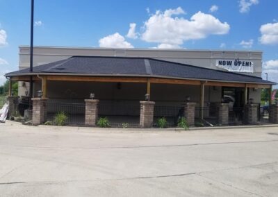 A newly opened restaurant with a "now open" banner, featuring a large parking lot and a brick column patio under a clear sky.