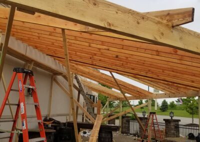 Construction of a wooden roof extension with metal supports and a ladder on a cloudy day.