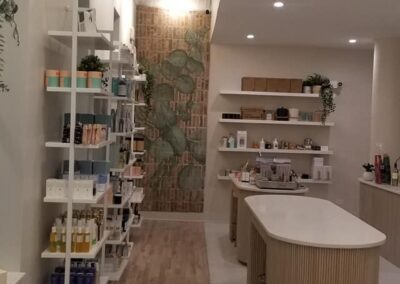 Interior of a modern boutique with shelves of beauty products, a central counter, tiled wall art, and elegant wooden flooring.