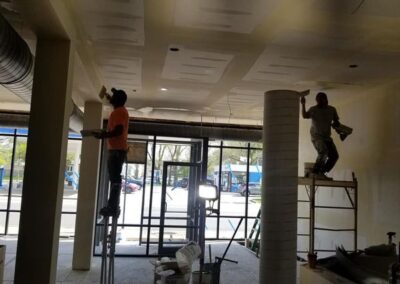 Two workers installing fixtures in a commercial building under renovation, with tools and construction materials around.