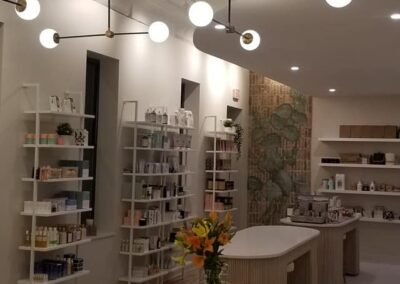 Modern retail store interior featuring circular wooden display tables, various products on white shelving, and round ceiling lights.