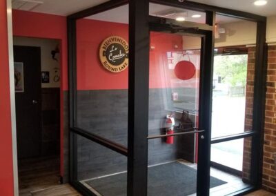 Entrance foyer with glass doors, a red welcome sign, and coat hooks on the wall in a well-lit commercial setting.