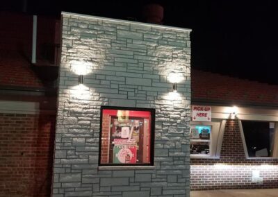 A photo of a brick building at night, featuring a window with a "taco casa" sign and a "pick-up here" window on the side.