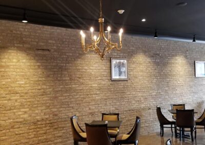 Interior of a restaurant with exposed brick walls, hanging chandeliers, and scattered dining tables.