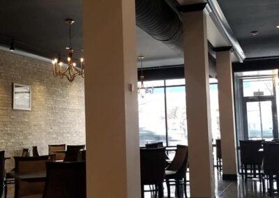 Interior of a modern restaurant featuring dark wood tables, glossy floors, brick walls, and a chandelier.