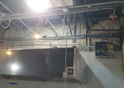 Industrial ventilation system with ductwork and electrical conduits installed on a ceiling, illuminated by overhead lights.