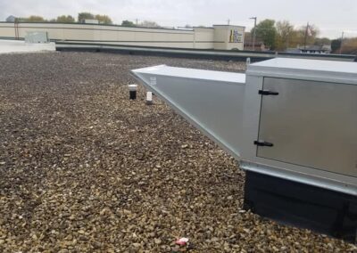 A technician works near a large metal hvac unit on a gravel-covered rooftop.