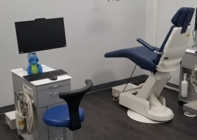 Modern dental clinic room with a dentist's chair, instruments, a computer on a desk, and a mounted monitor.