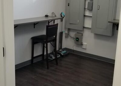 A minimalist office space with a desk, chair, and several electrical panels on the wall, featuring gray flooring and walls.