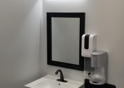 A modern bathroom featuring a white sink, rectangular mirror with an overhead light, a soap dispenser, and a step stool.