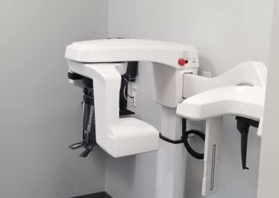 A panoramic dental x-ray machine in a modern clinic room with gray flooring and light gray walls.