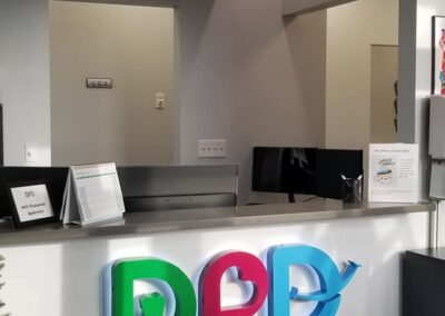 Modern office reception area with a colorful 'dpd' logo on the front desk, computers, and informational signage.