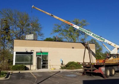 A mobile crane repairing a roof on a small commercial building under clear blue skies.