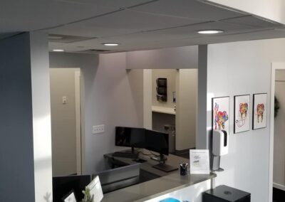 Modern office reception area with a clean design, featuring a desk with a computer, framed art on the wall, and a coffee machine in the background.