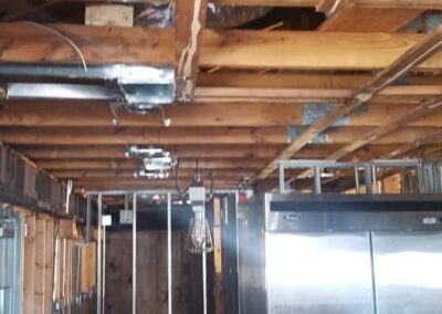 Unfinished interior of a building showing exposed wooden beams, ductwork, and a metal refrigerator.