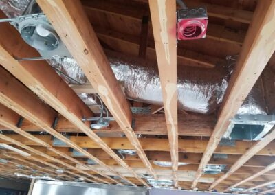 Exposed hvac ducts and electrical wires in an unfinished ceiling with wooden beams and insulation.