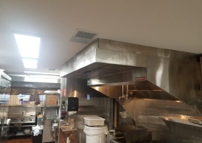 Interior of a commercial kitchen with stainless steel appliances, exhaust hoods, and scattered utensils.