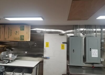 Interior of a commercial kitchen showing a meat slicer, storage shelves, and electrical panels.