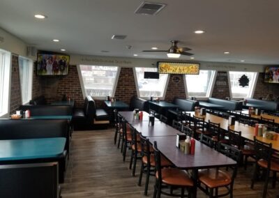 Interior of a casual restaurant with black booths, wooden tables, stools, and various wall decorations, including sports memorabilia.