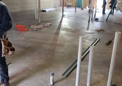 Interior of a building under construction with exposed brick walls, visible construction materials, and a worker in the background.