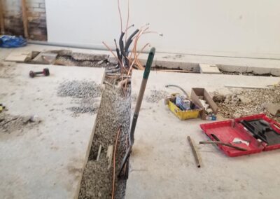 Exposed electrical wires and construction tools on a demolished concrete floor inside a building.