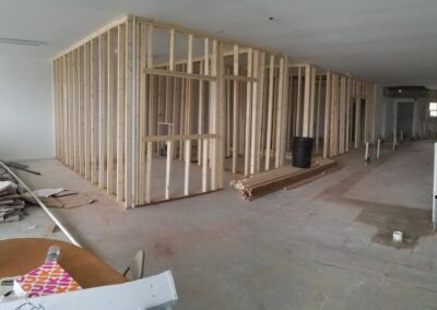 Interior construction site with exposed wooden framing for rooms and materials scattered on concrete floor.