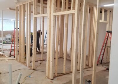 Construction workers building a wooden frame for a room inside a building, with tools and ladders visible on the site.