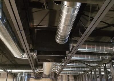 Metal ductwork and piping suspended from a black ceiling in an industrial setting.