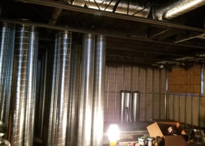 An industrial workspace with exposed ventilation ducts and construction materials illuminated by a floor lamp.