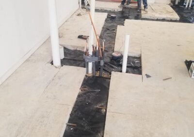 A worker installs plumbing through a concrete floor in a building under construction.