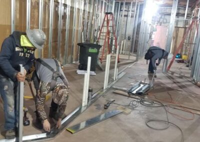 Three construction workers install metal framing and ductwork in a building under renovation.