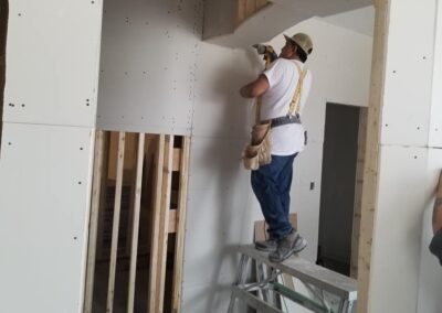 A construction worker using a drill on drywall in a partially completed building interior.