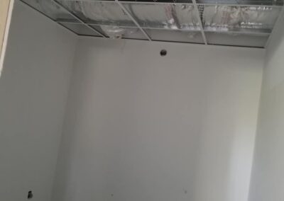 Exposed air ducts and electrical outlets in an unfinished room with white walls and a missing ceiling panel.