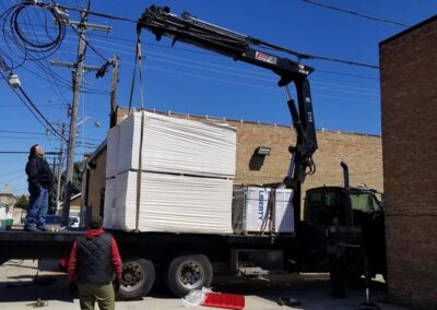 A crane unloading materials from a truck observed by two men, with overhead wires and clear skies in the background.