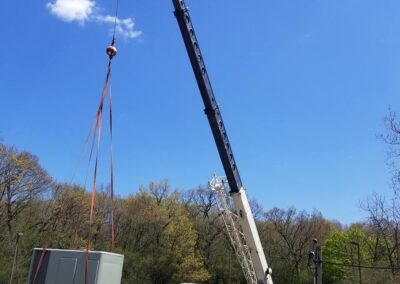 A crane lifting a large metallic box at a construction site under a clear blue sky.