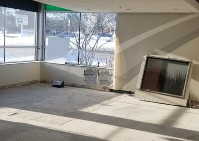 Interior of a vacant room under renovation with exposed ceiling, bare floors, and a large window letting in natural light.