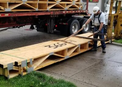 A worker unloading large wooden planks from a flatbed truck on a city street.