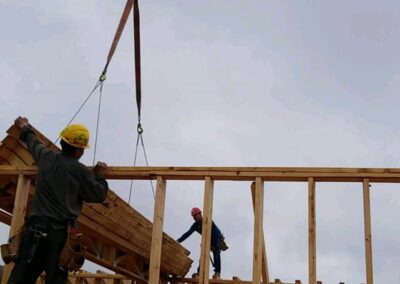 Construction workers assembling a wooden building frame, with one guiding a crane carrying lumber.