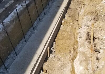 Construction site showing a newly built concrete foundation with exposed rebar in a trench.