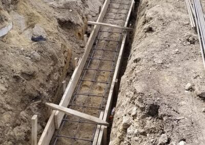 A construction site with a deep, narrow trench reinforced by wooden frames and steel rebar, prepared for concrete pouring.