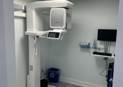 A dental panoramic x-ray machine in a clinical setting with light blue walls and gray tiled flooring.