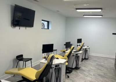 Interior of a modern dental clinic with multiple dental chairs equipped with computers and monitors, under bright ceiling lights.