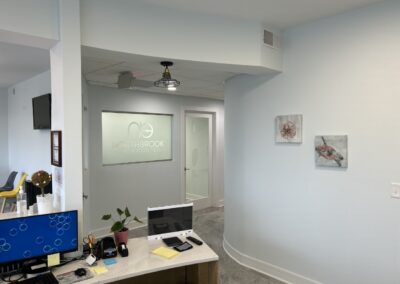 Modern dental office reception area with clean design, a desk with computer and files, artwork on walls, and a glass door with the logo "northbrook orthodontics.