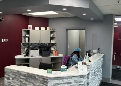 Interior of a modern office reception with grey stone counters, burgundy walls, and a person seated at a desk.