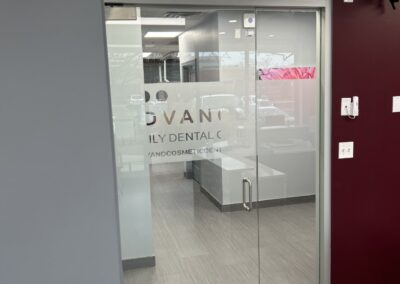 Interior view of a dental clinic, showcasing a glass entrance door with frosted clinic name, and a waiting area visible through the door.