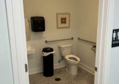 View of a small, accessible bathroom with open door, featuring a toilet, sink, and safety grab bars.